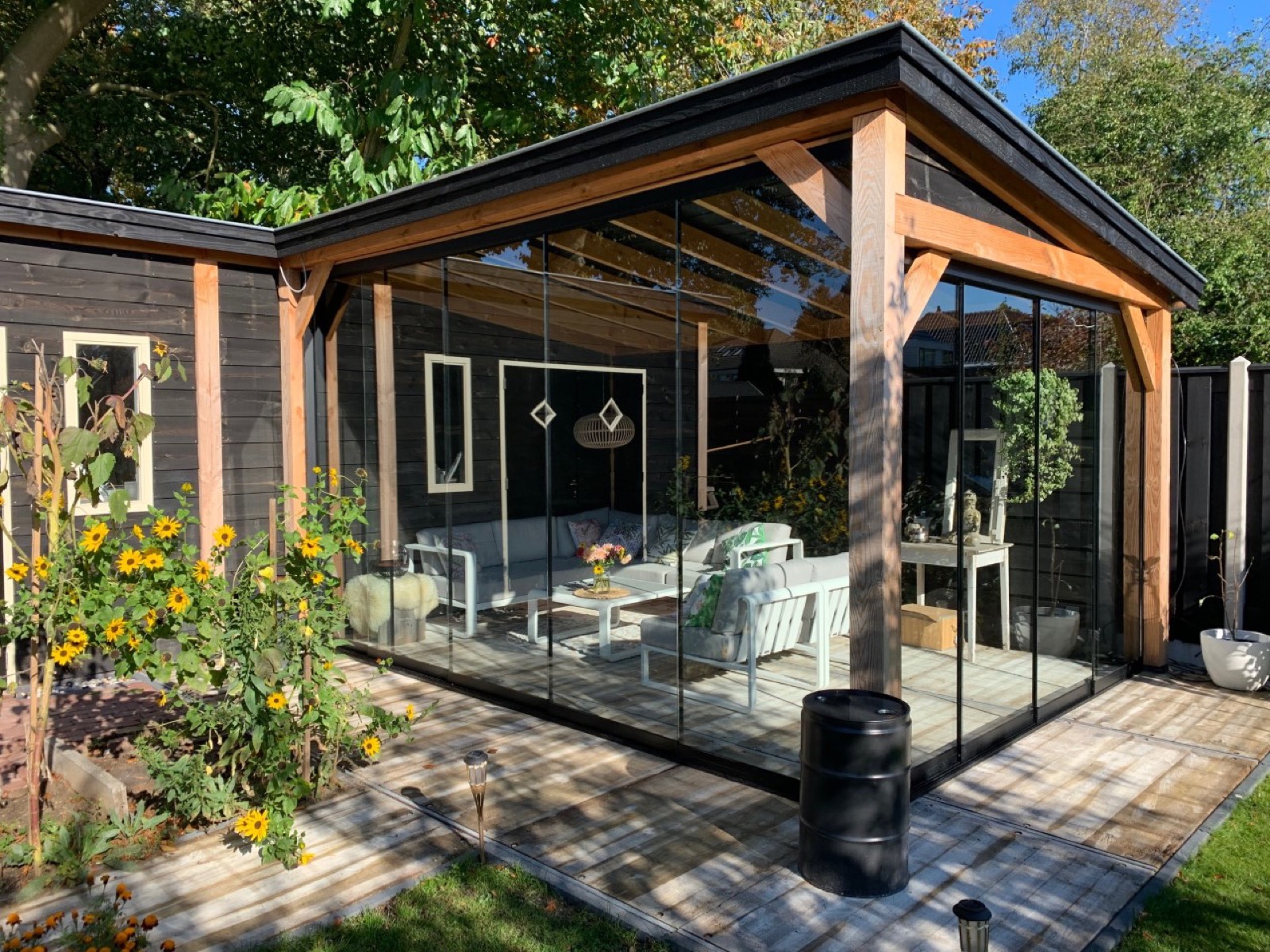 Glazen schuifwanden met zwart frame sluiten een overkapping met loungeset af