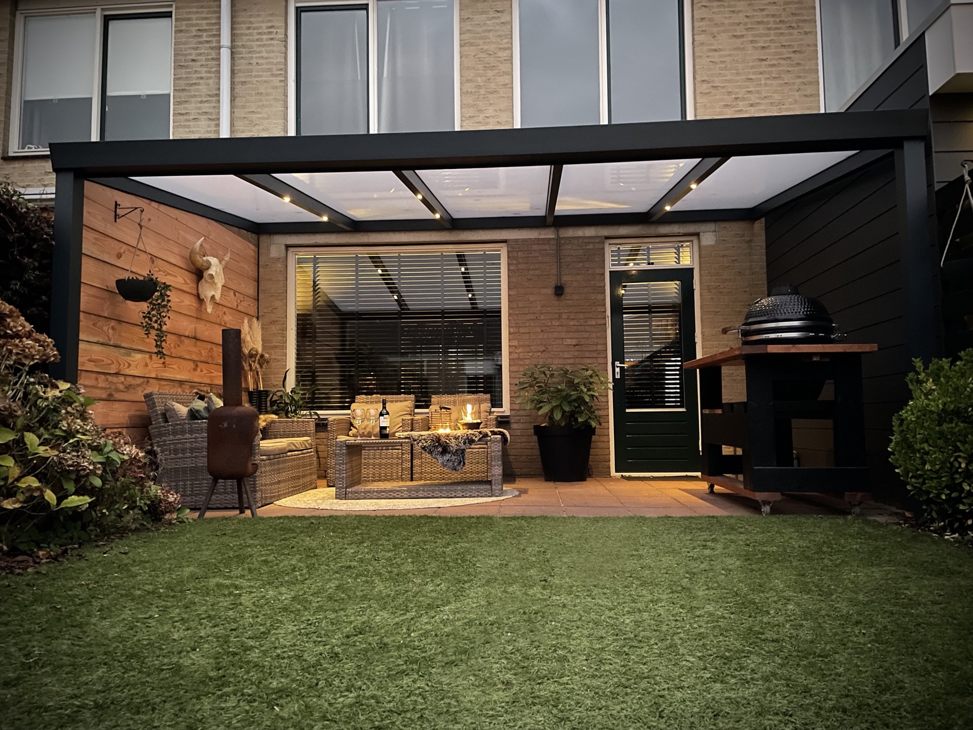 Aluminium terrasoverkapping aan huis met glasdak en sfeerverlichting in de avond